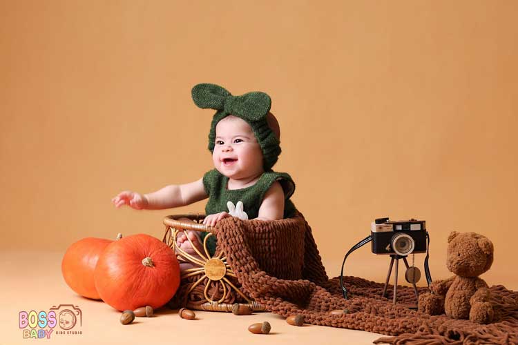 یده عکاسی نوزاد پاییزی با لباس کرم و دکور برگهای نارنجی