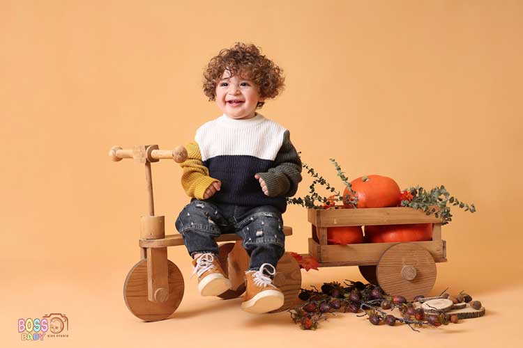 یده عکاسی نوزاد پاییزی با لباس کرم و دکور برگهای نارنجی